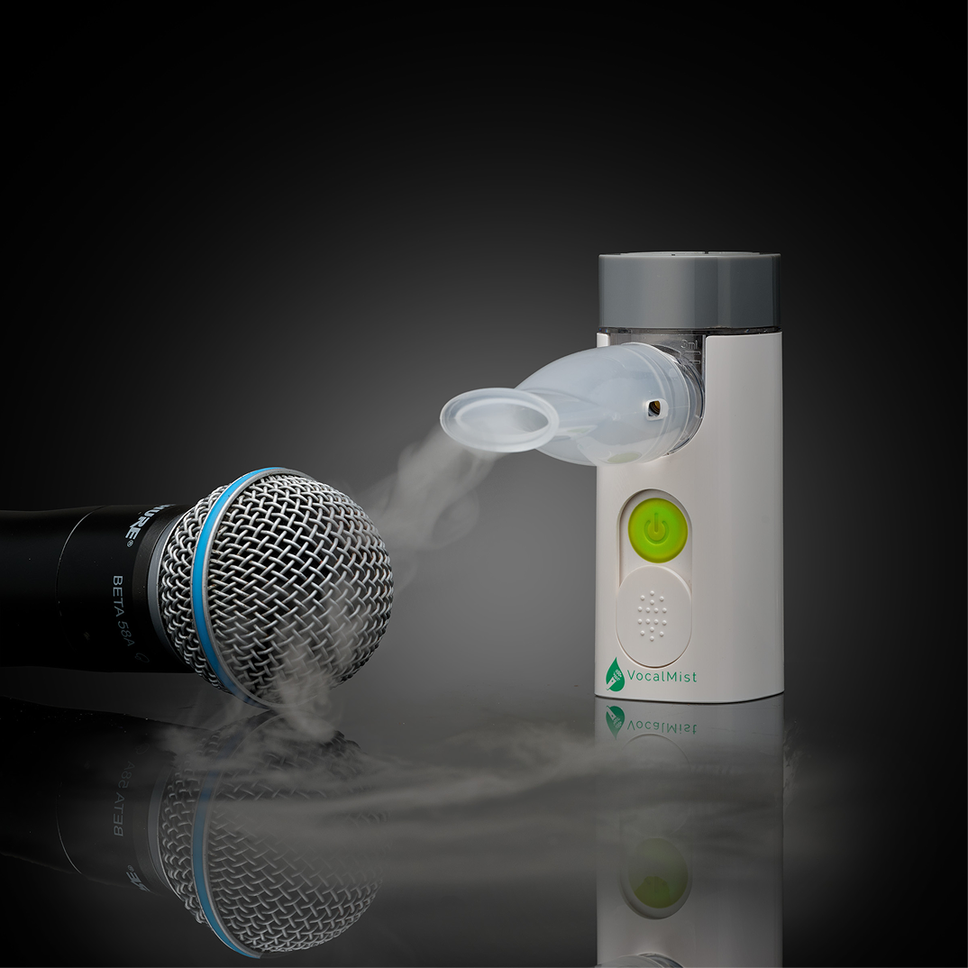 VocalMist Portable Nebulizer — device releasing mist beside a microphone on dark reflective glass.