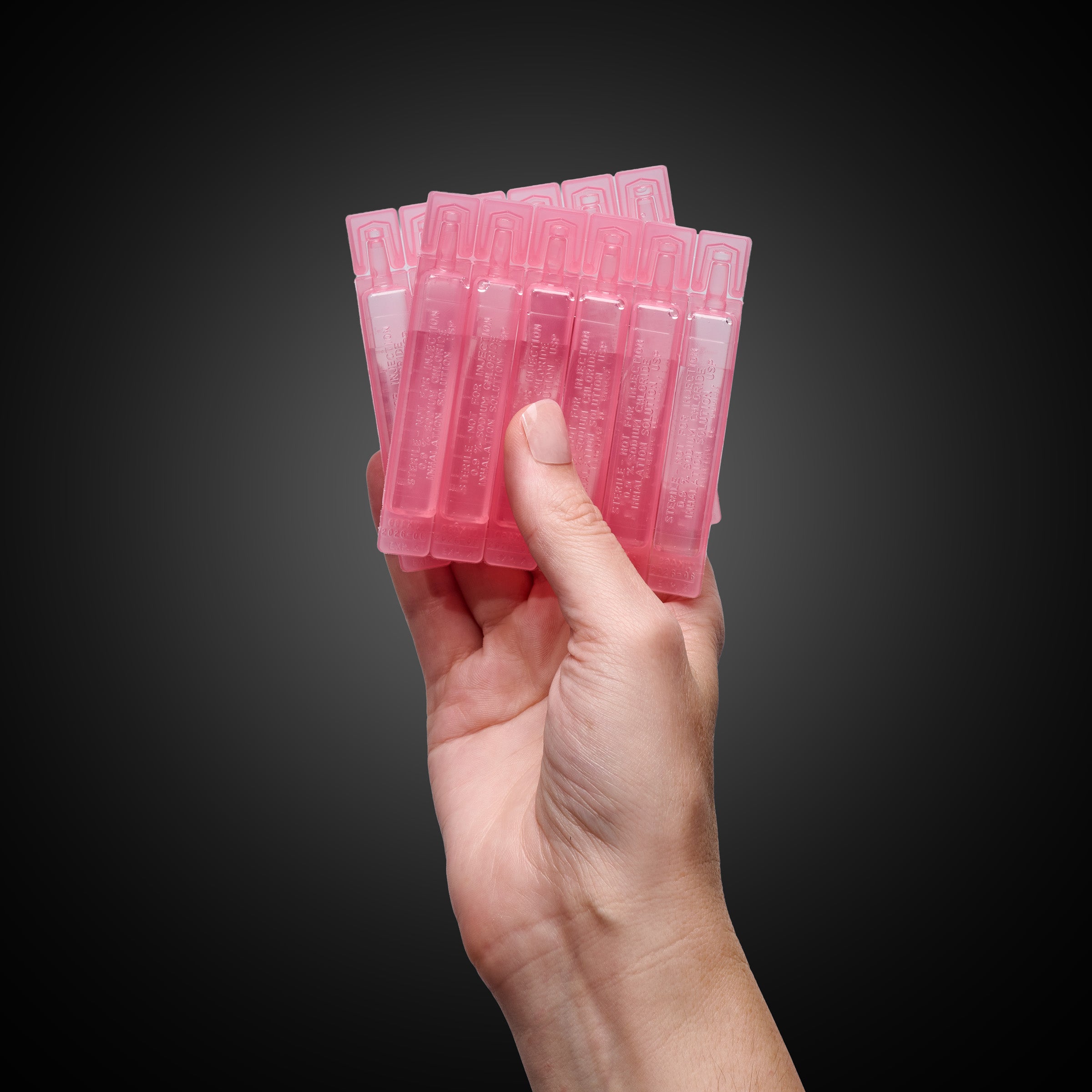 VocalMist Hydration Formula — pink saline vials fanned in hand against a dark studio background.