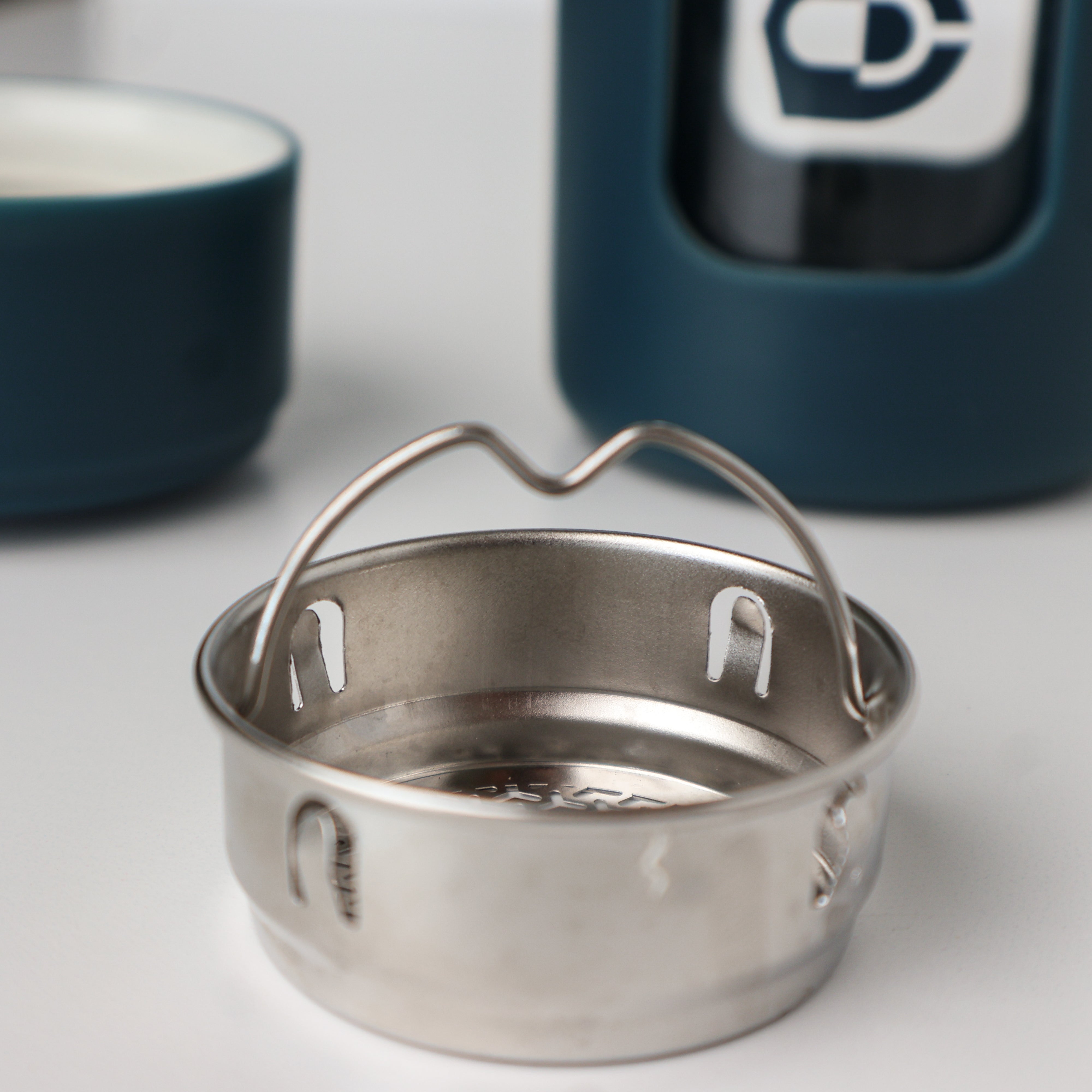 VocalGuard Glass Bottle — close-up of the stainless steel inner basket with the teal bottle behind.