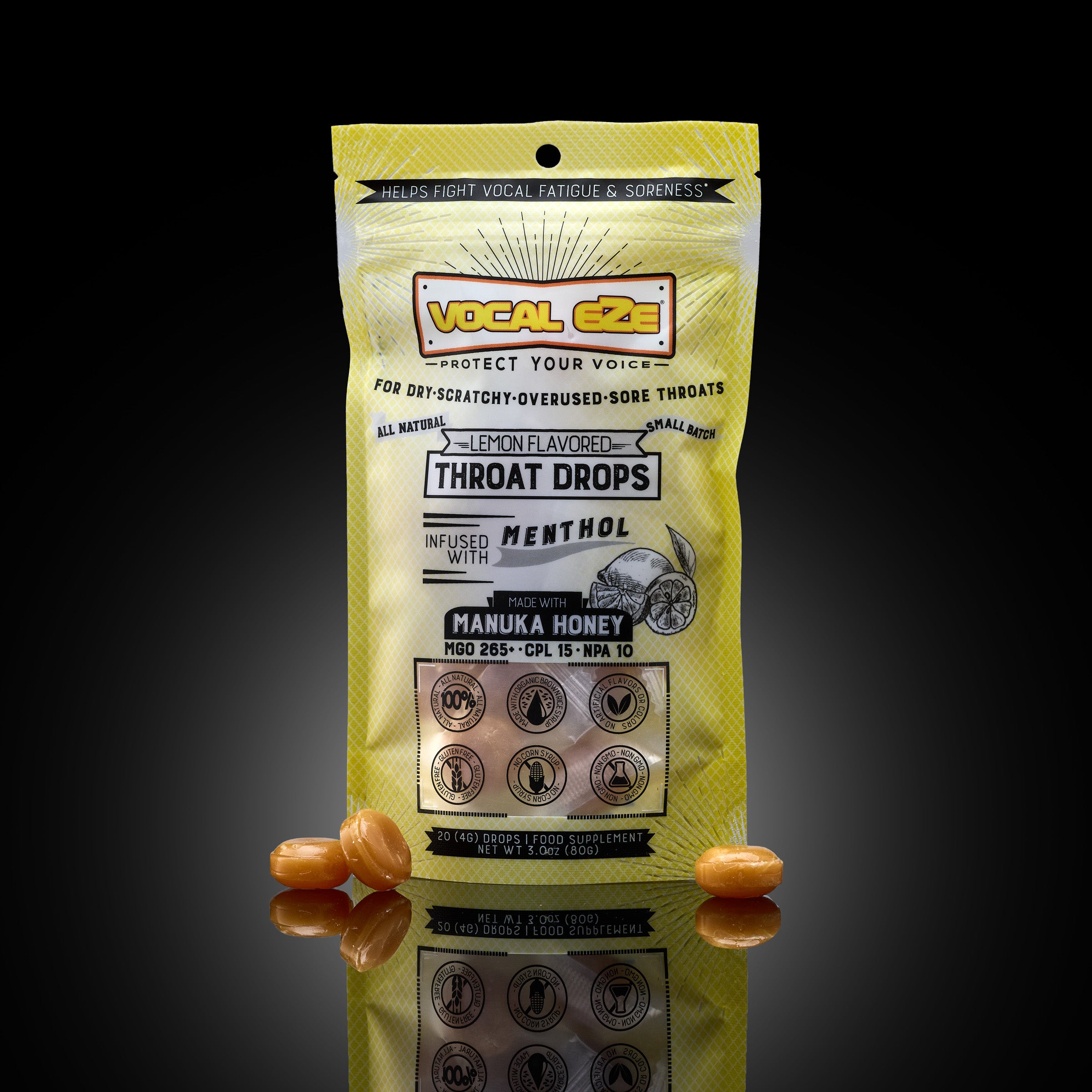 Vocal Eze Lemon Drops — pouch with honey lozenges beside it on dark reflective glass.