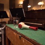 Breather Voice respiratory trainer lying on the felt top of a rehearsal-room piano beside a glass of water.