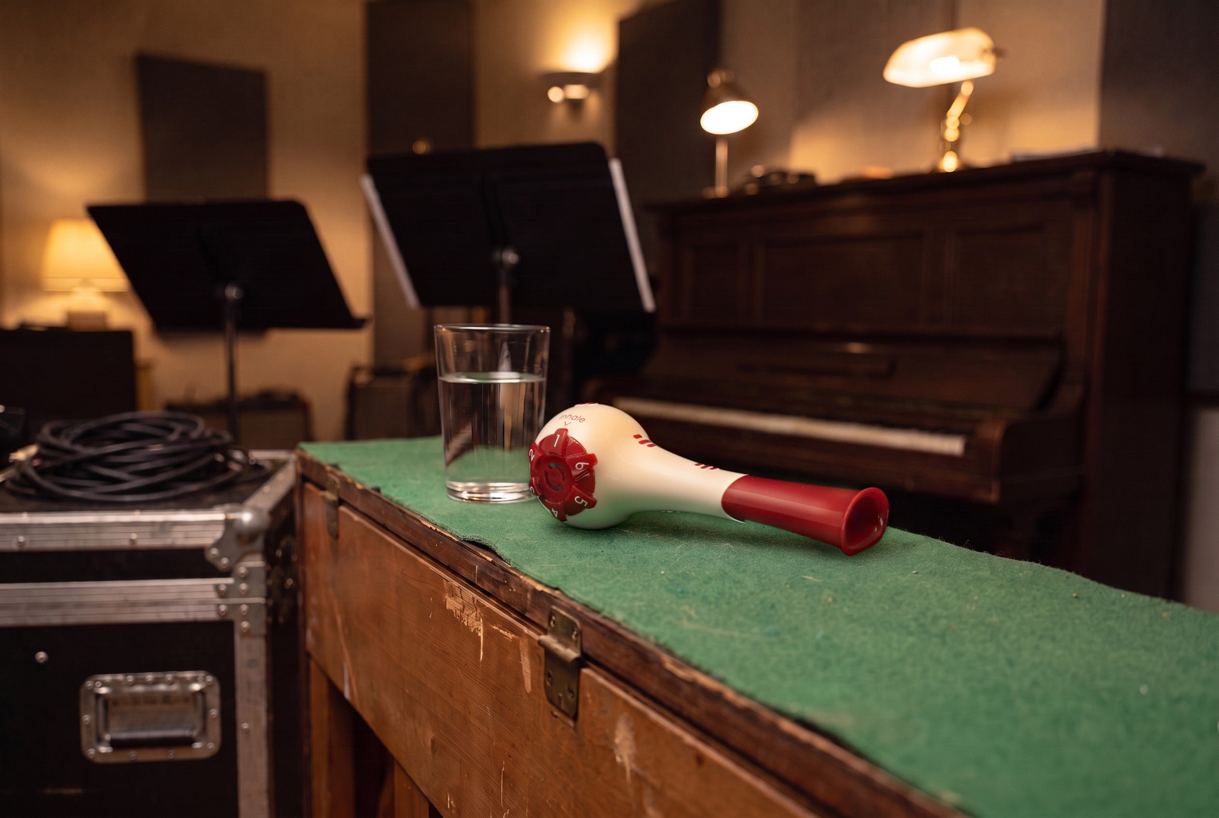 Breather Voice respiratory trainer lying on the felt top of a rehearsal-room piano beside a glass of water.