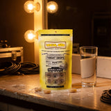 Vocal Eze Lemon Drops pouch on a dressing-room counter under mirror lights, lozenges in front.