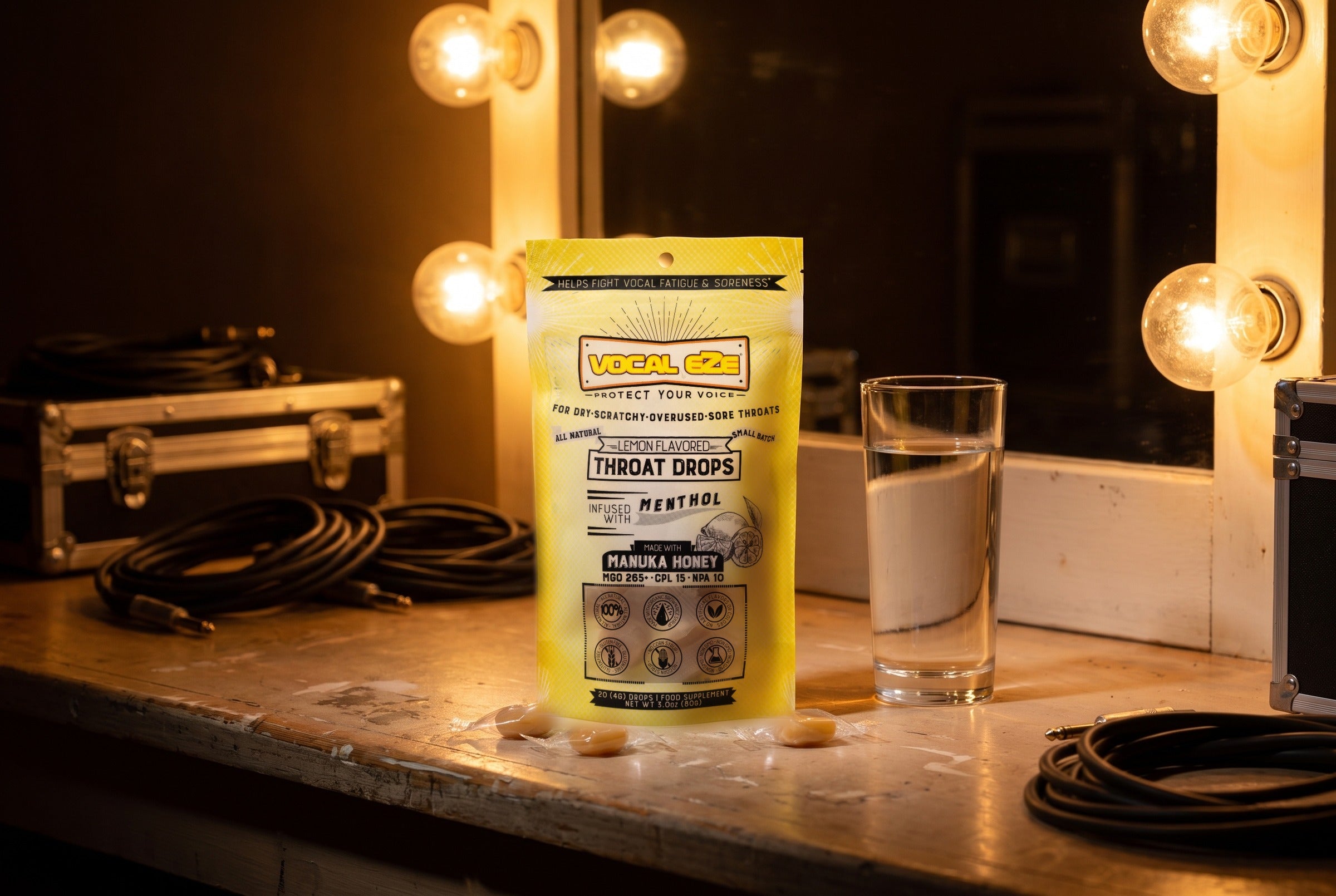 Vocal Eze Lemon Drops pouch on a dressing-room counter under mirror lights, lozenges in front.