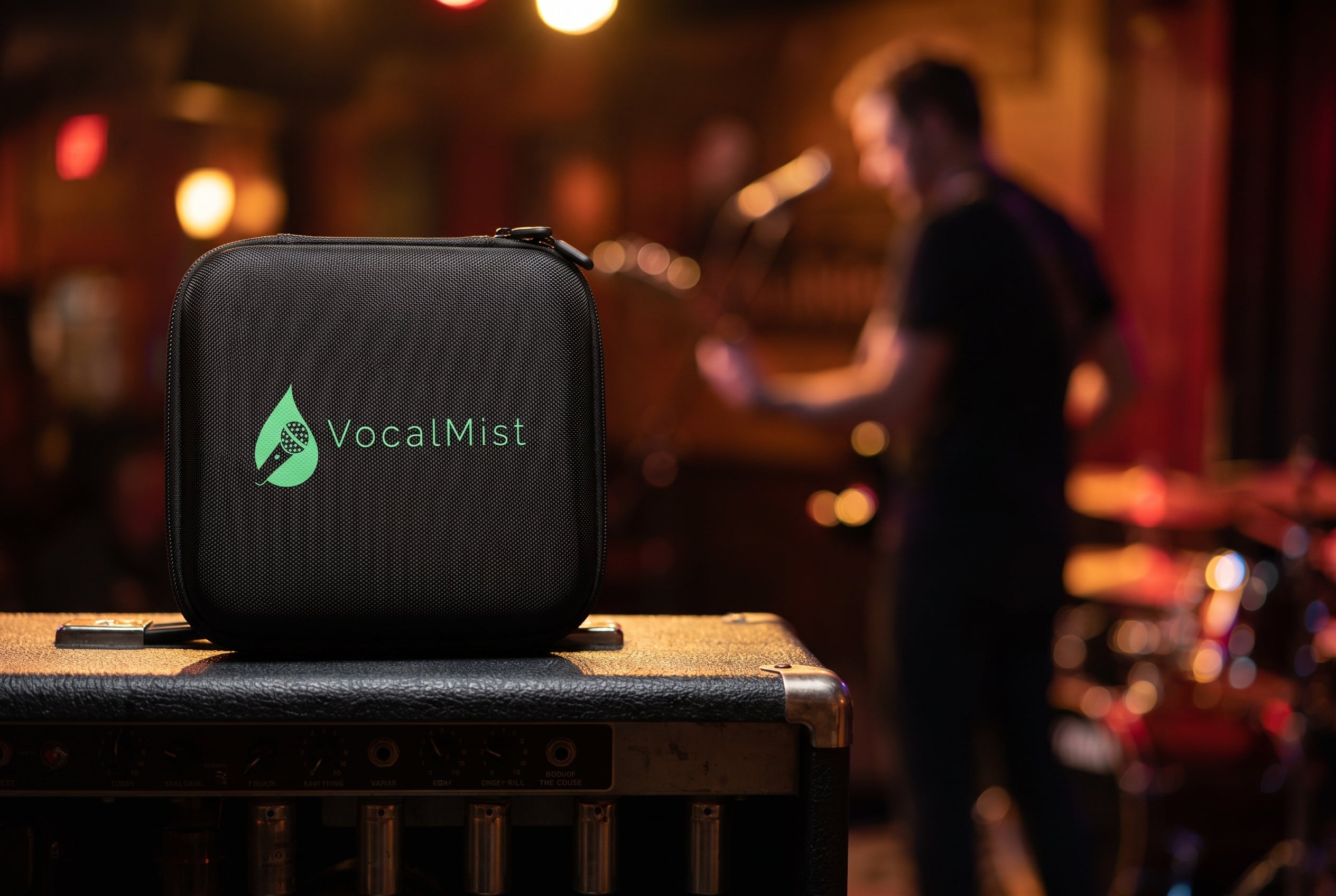 VocalMist carrying case on a guitar amp during rehearsal, guitarist in the background.