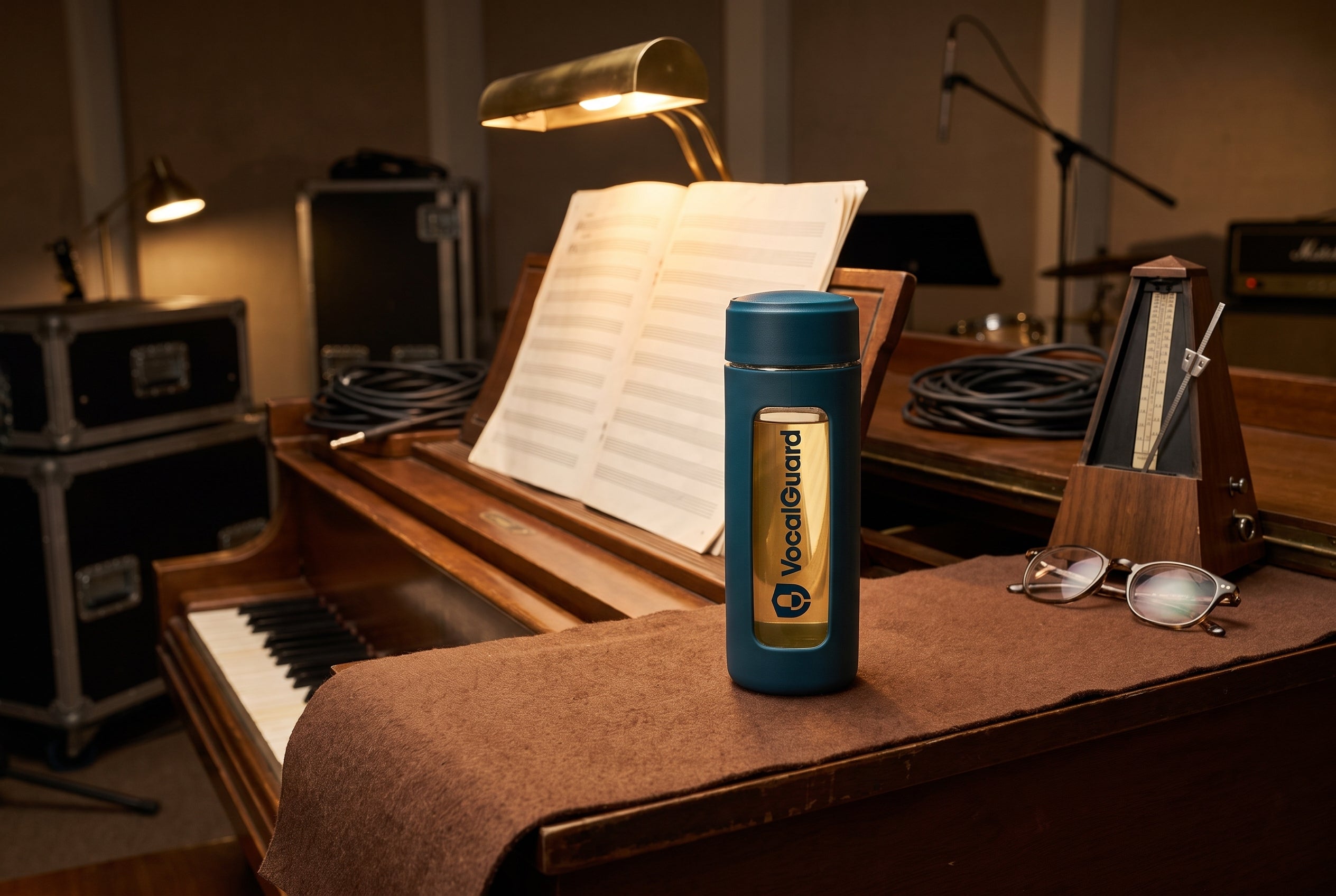 VocalGuard glass bottle on a piano-top felt runner in a rehearsal room.