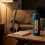 VocalGuard glass bottle on a songwriting coffee table next to an acoustic guitar.