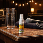 Vocal Eze Throat Spray on a green-room side table beside a glass of water and a microphone.
