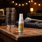 Vocal Eze Throat Spray on a green-room side table beside a glass of water and a microphone.