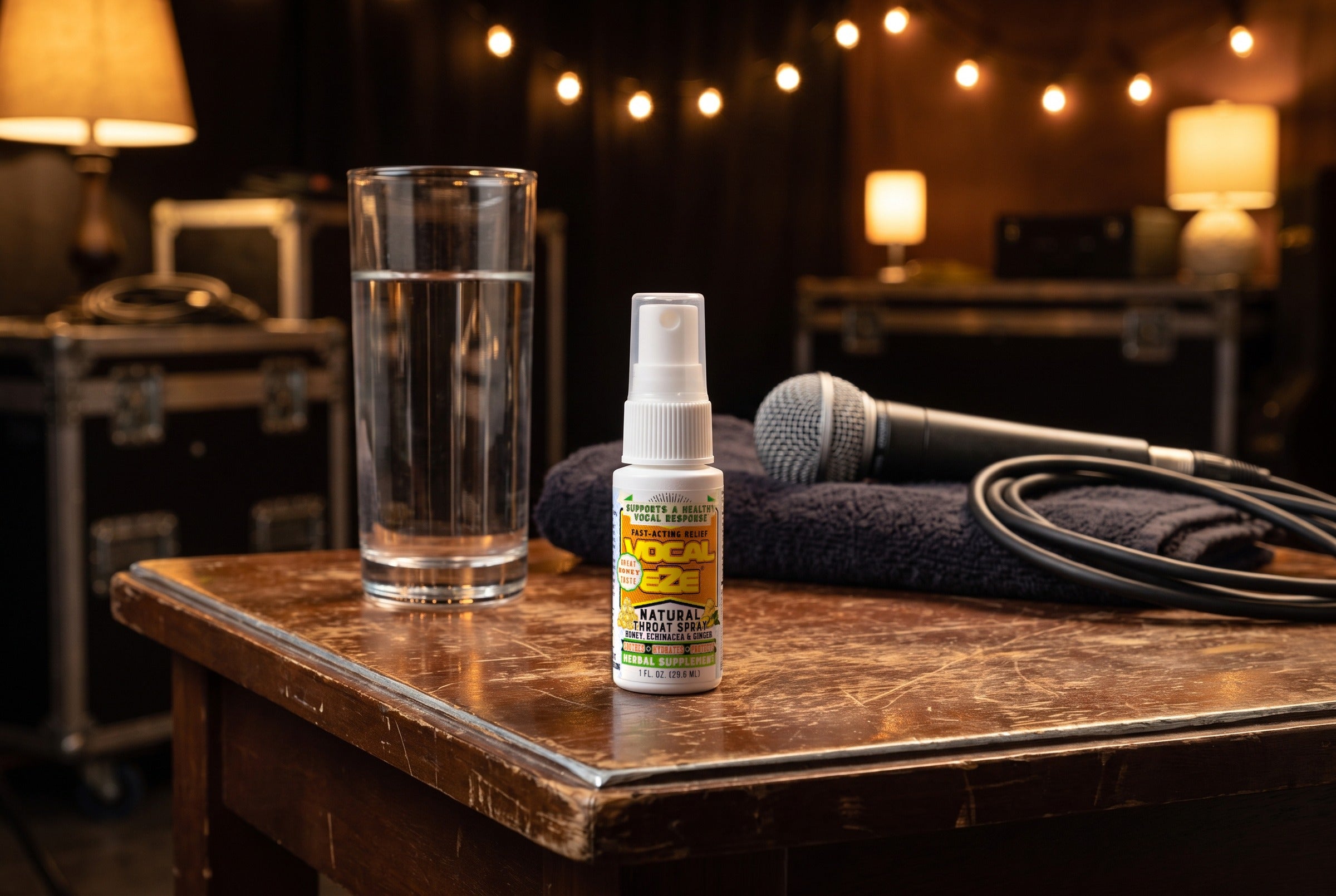 Vocal Eze Throat Spray on a green-room side table beside a glass of water and a microphone.