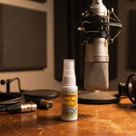 Vocal Eze Throat Spray on a voice-over booth desk beneath a condenser microphone.