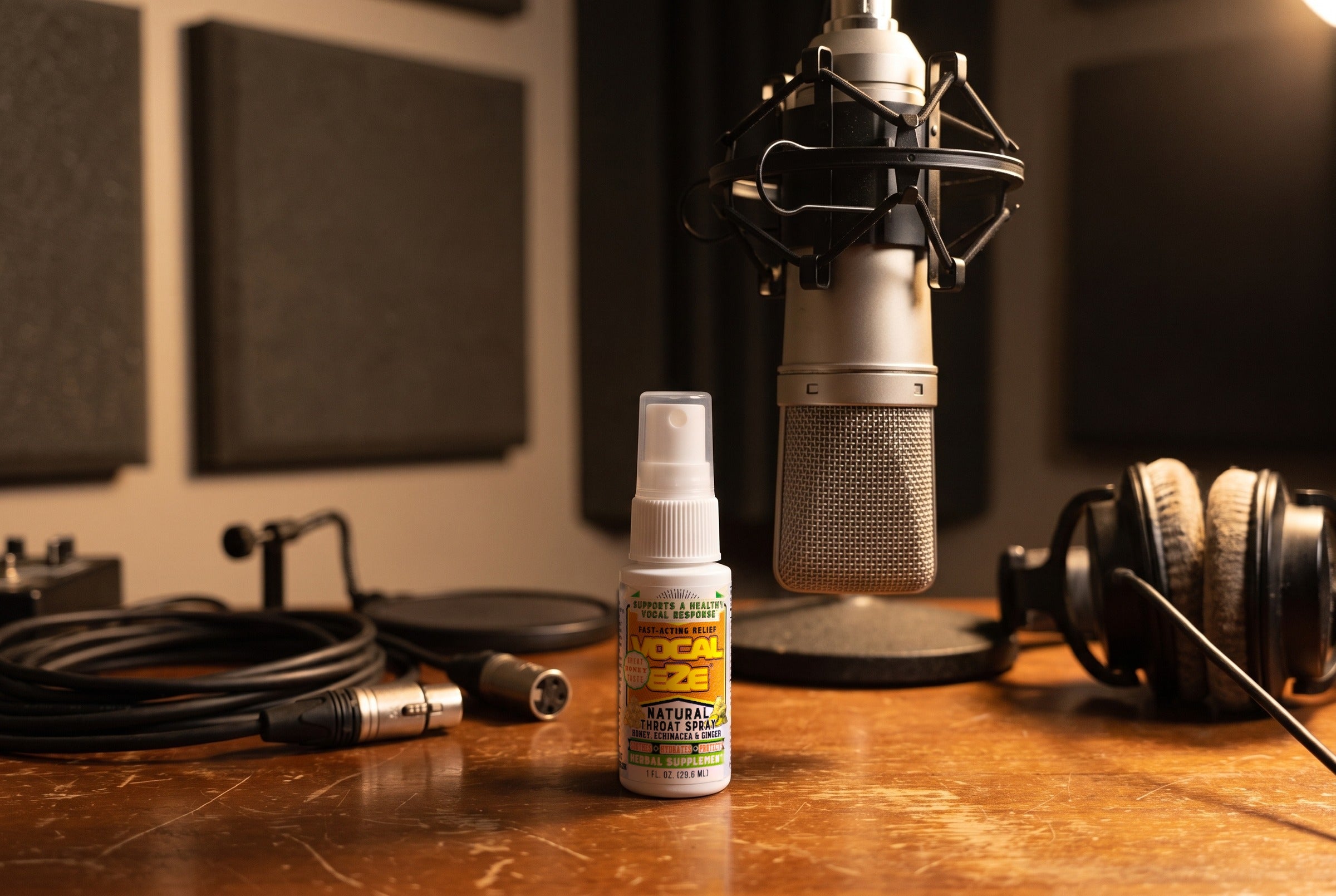 Vocal Eze Throat Spray on a voice-over booth desk beneath a condenser microphone.